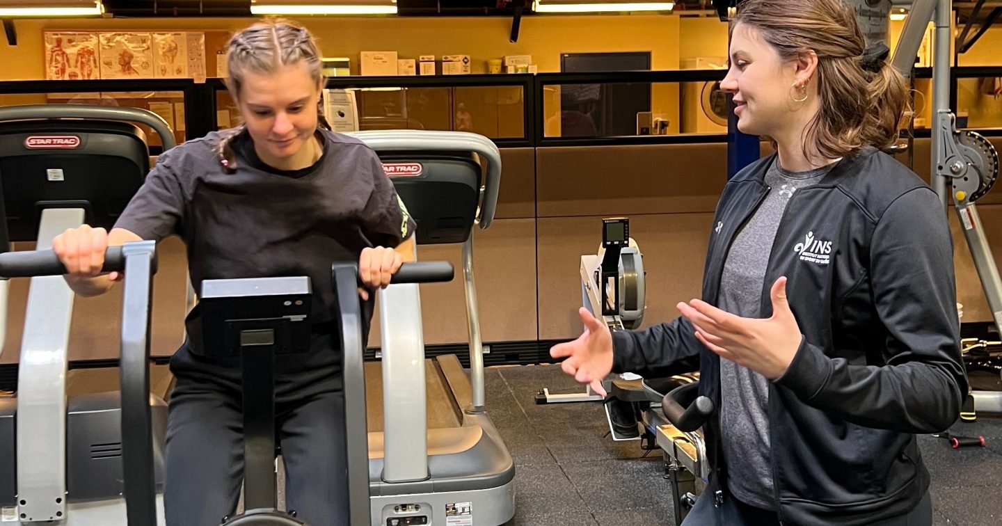 Ioana Gheta, préparatrice physique de l'INS Québec, prodigue ses conseils à une artiste du Cirque du Soleil, qui est sur un vélo stationnaire.