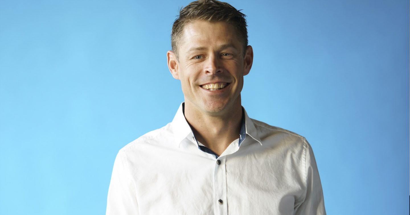 Portrait de Benoît-Hugo, souriant, portant une chemise blanche, sur un fond bleu ciel.